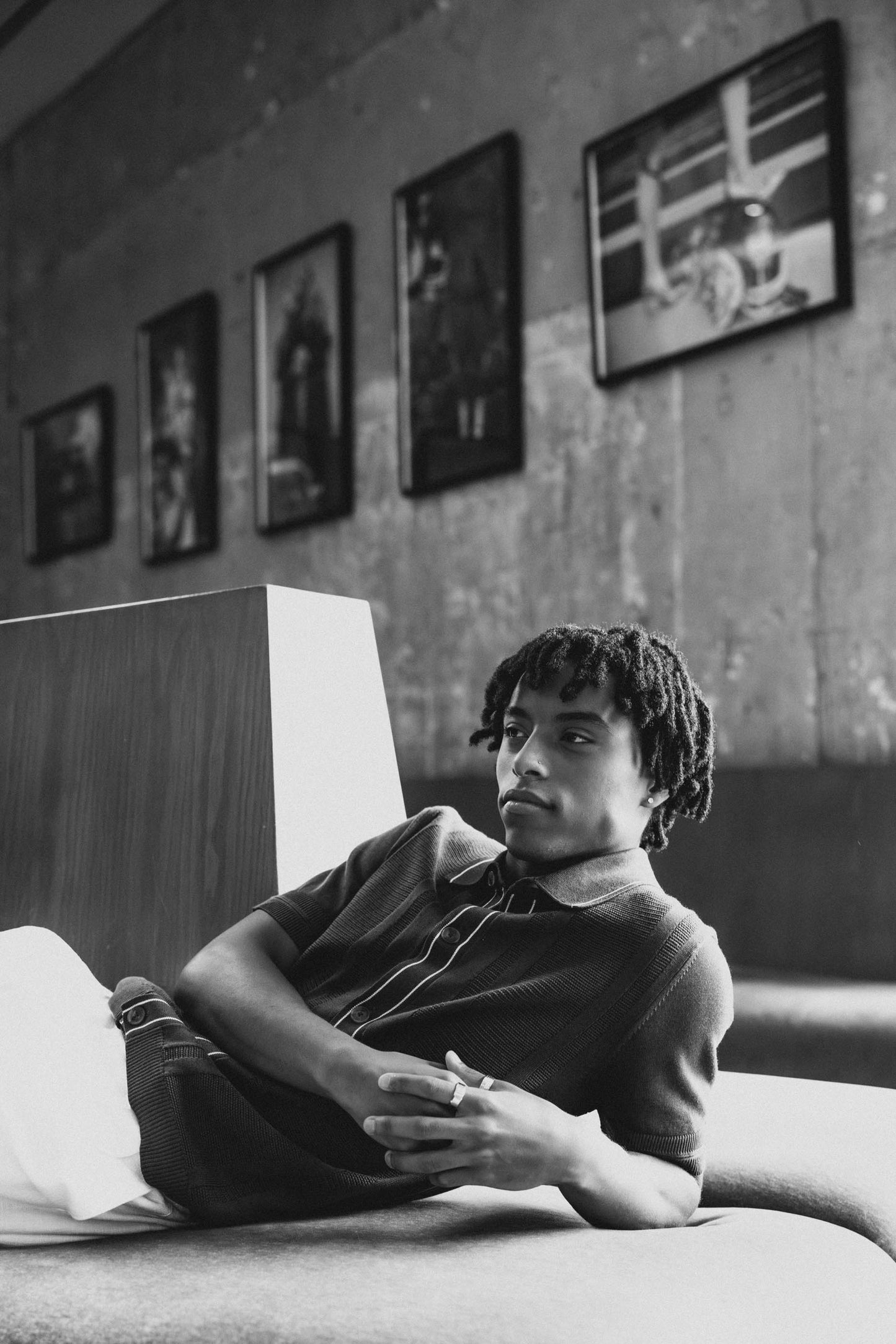 Black and white image of Mekonnen Knife laying back on a couch in a room with framed pictures on the wall.