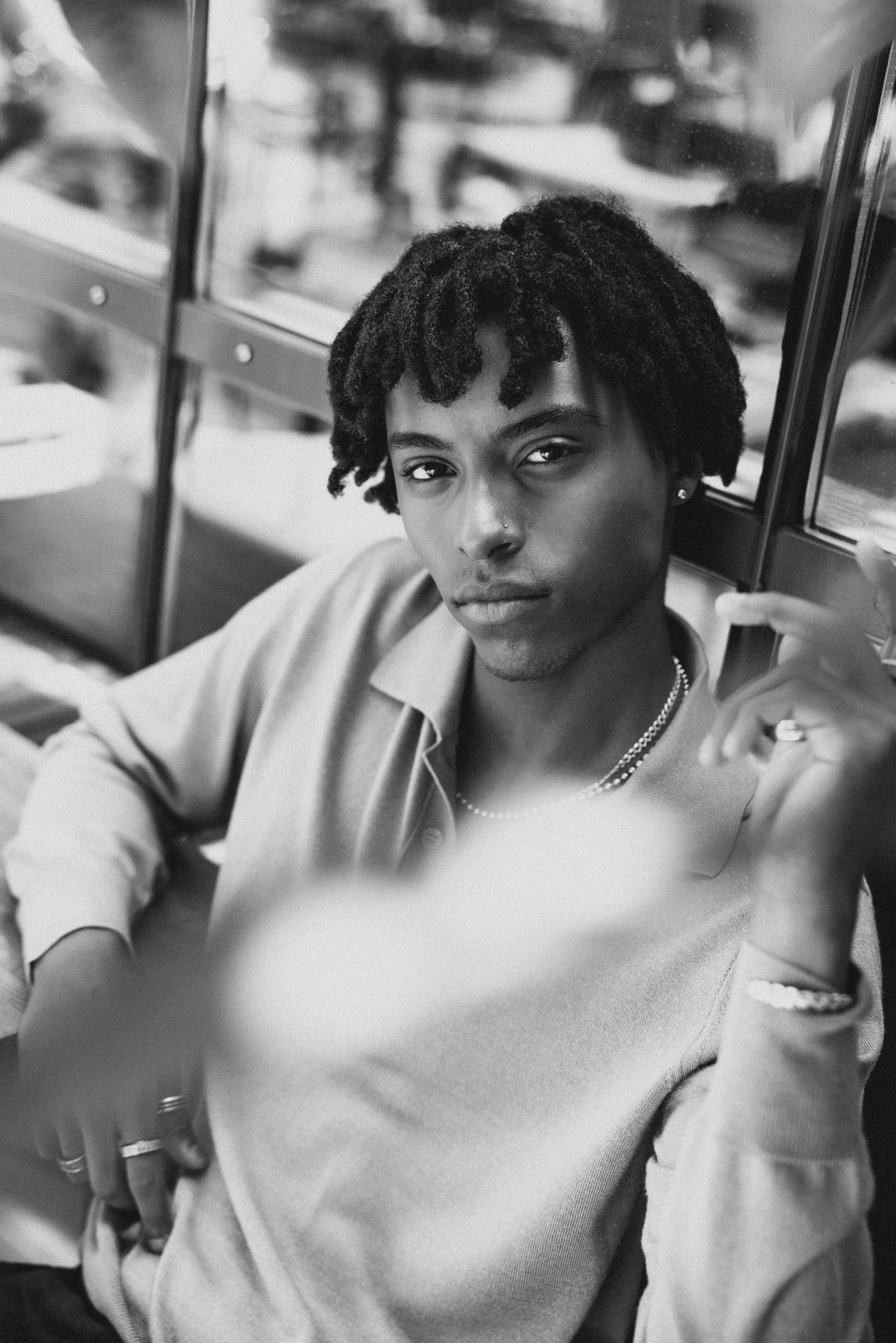 Black and white image of Mekonnen Knife sitting against a glass and metal wall in an outdoor urban setting.