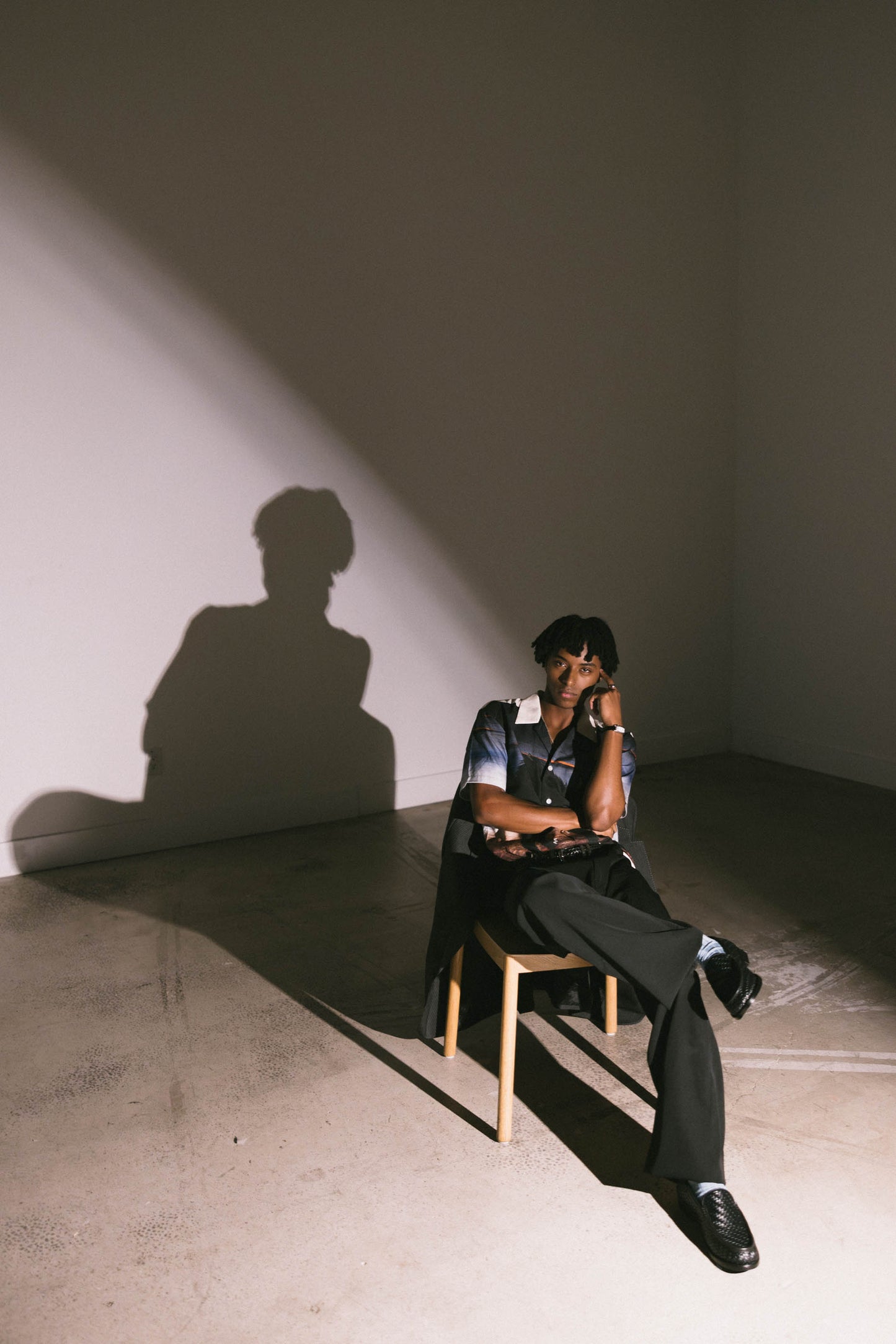 Mekonnen Knife sitting on a chair with a dramatic light casting a shadow on the wall.