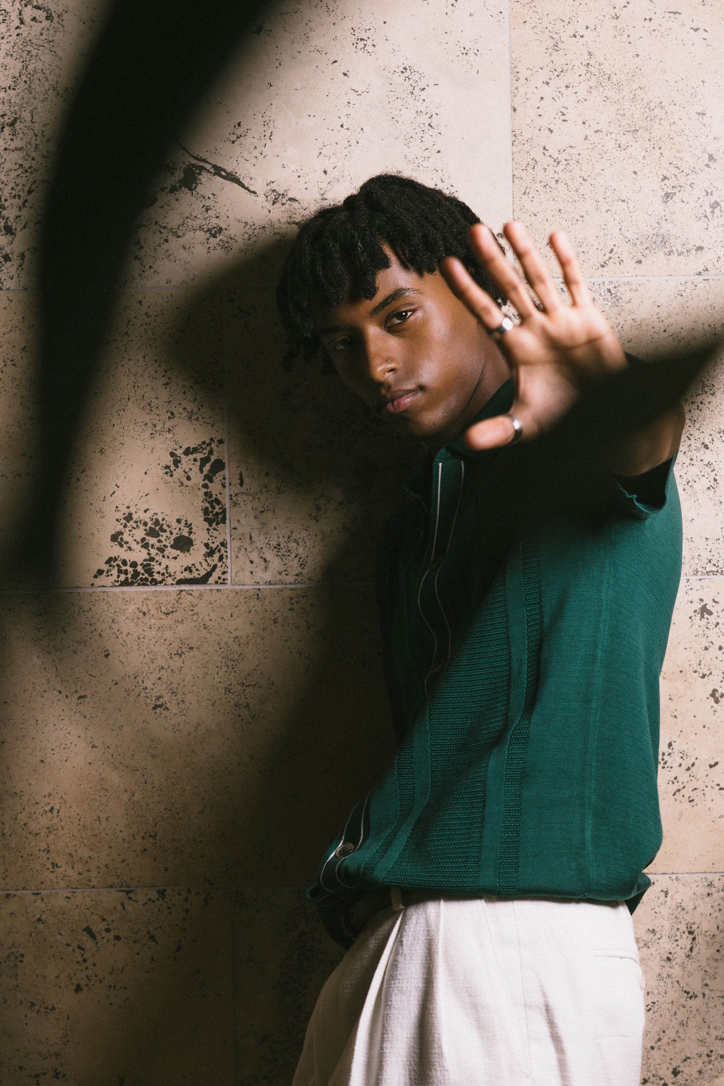 Mekonnen Knife wearing a green sweater and white pants against a textured wall.